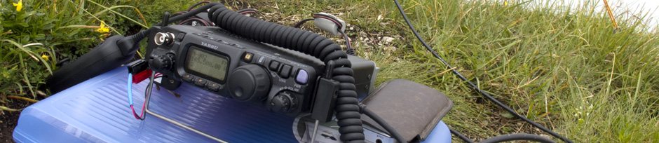 Tragbarer Kurzwellen-Transceiver mit Mikrofon und Akku auf einer Isomatte im Gras