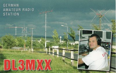 QSL-Karte DL3MXX: Antennenanlage vor Gewitterhimmel, eingesetzt ein Foto des Operators mit Kopfhörer